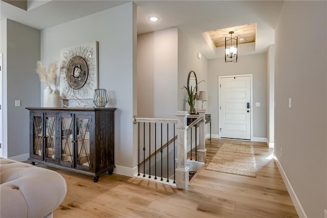 foyer featuring light wood-type flooring, a raised ceiling, and a notable chandelier