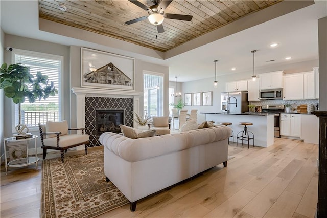 living room featuring light wood-type flooring, a raised ceiling, and a tile fireplace