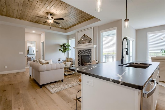 kitchen with a tile fireplace, light hardwood / wood-style flooring, decorative light fixtures, a center island with sink, and sink