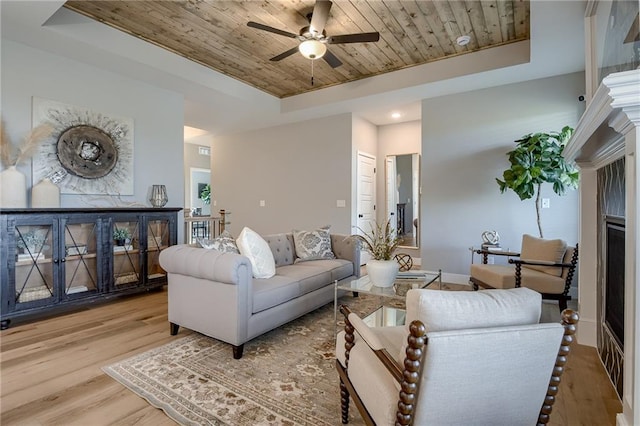 living room featuring a fireplace, wooden ceiling, a tray ceiling, ceiling fan, and light hardwood / wood-style flooring