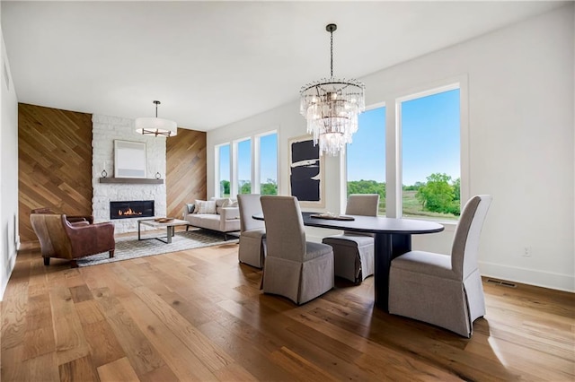 dining room with wood-type flooring, a stone fireplace, a notable chandelier, and wood walls