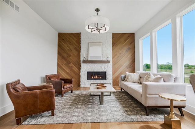 living room featuring a healthy amount of sunlight, a stone fireplace, wood walls, and hardwood / wood-style flooring