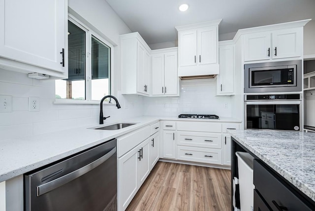 kitchen featuring sink, appliances with stainless steel finishes, light hardwood / wood-style flooring, backsplash, and white cabinetry