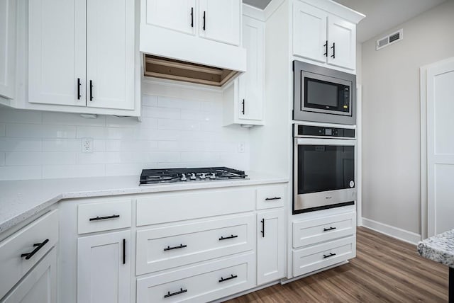 kitchen featuring appliances with stainless steel finishes, dark wood-type flooring, light stone counters, backsplash, and white cabinetry