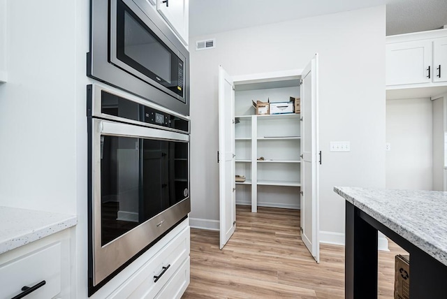 kitchen with light stone countertops, appliances with stainless steel finishes, light hardwood / wood-style floors, and white cabinetry