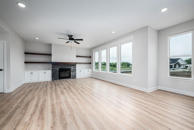 unfurnished living room with a stone fireplace, ceiling fan, and light wood-type flooring