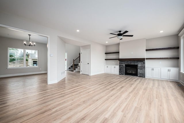 unfurnished living room with a fireplace, ceiling fan with notable chandelier, and light hardwood / wood-style flooring