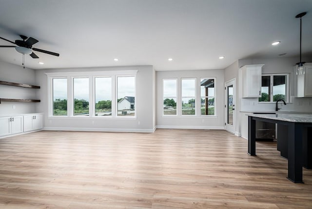 unfurnished living room featuring plenty of natural light, light hardwood / wood-style floors, ceiling fan, and sink