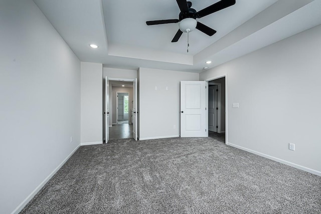 unfurnished bedroom with dark carpet, a raised ceiling, and ceiling fan