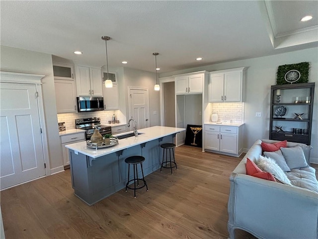 kitchen featuring white cabinets, appliances with stainless steel finishes, pendant lighting, and light hardwood / wood-style flooring