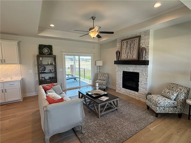 living room with a stone fireplace, light hardwood / wood-style floors, ceiling fan, and a raised ceiling