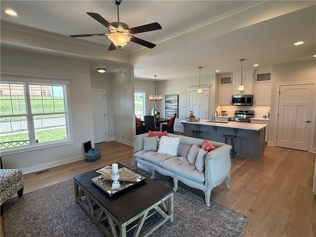 living room featuring ornamental molding, sink, ceiling fan with notable chandelier, and hardwood / wood-style flooring