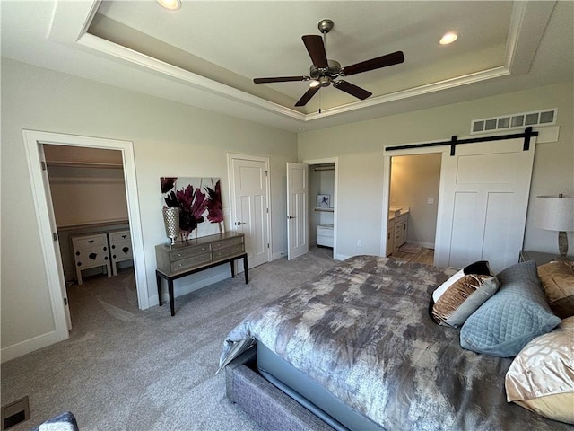 carpeted bedroom with ceiling fan, a tray ceiling, connected bathroom, and a barn door