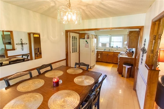 dining area with sink, a notable chandelier, light hardwood / wood-style floors, and a textured ceiling