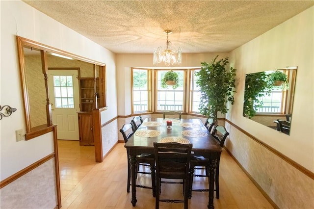 dining area featuring a notable chandelier, a textured ceiling, and light wood-type flooring