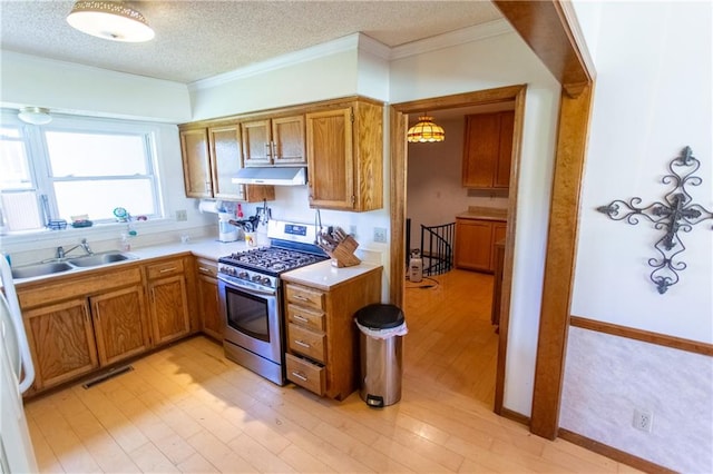 kitchen with pendant lighting, light hardwood / wood-style floors, a textured ceiling, gas stove, and sink