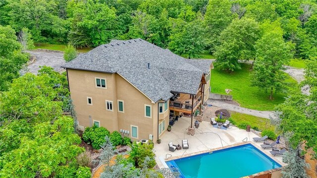 29800 E 65th St, Blue Springs, MO 64014 - rear view of house featuring stucco siding, a shingled roof, a patio, an outdoor pool, and a wooded view