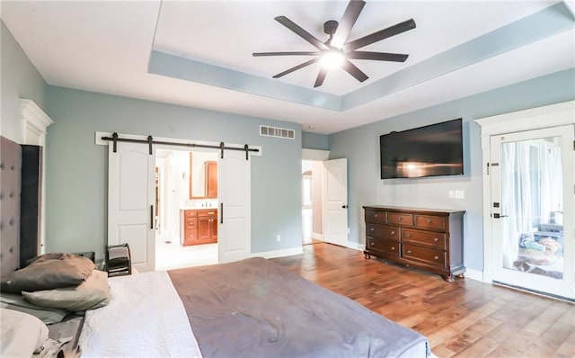 29800 E 65th St, Blue Springs, MO 64014 - bedroom featuring wood finished floors, a barn door, a tray ceiling, baseboards, and ceiling fan