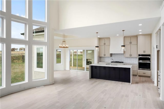 kitchen featuring stainless steel double oven, a wealth of natural light, a center island with sink, and pendant lighting