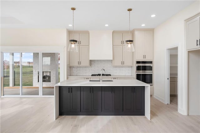 kitchen featuring a center island with sink, appliances with stainless steel finishes, hanging light fixtures, and light hardwood / wood-style floors