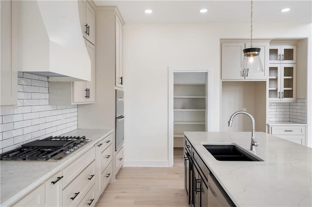 kitchen with appliances with stainless steel finishes, sink, pendant lighting, light stone counters, and premium range hood