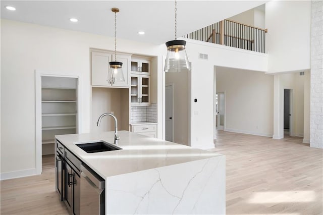 kitchen with a kitchen island with sink, sink, pendant lighting, stainless steel dishwasher, and light stone counters