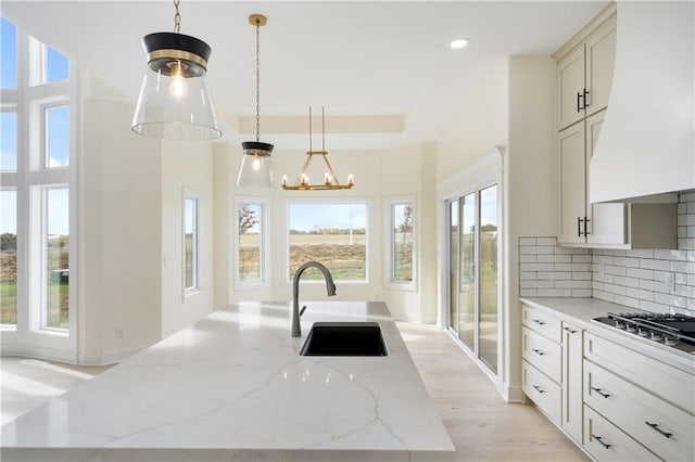 kitchen with light hardwood / wood-style flooring, custom range hood, sink, light stone countertops, and decorative light fixtures