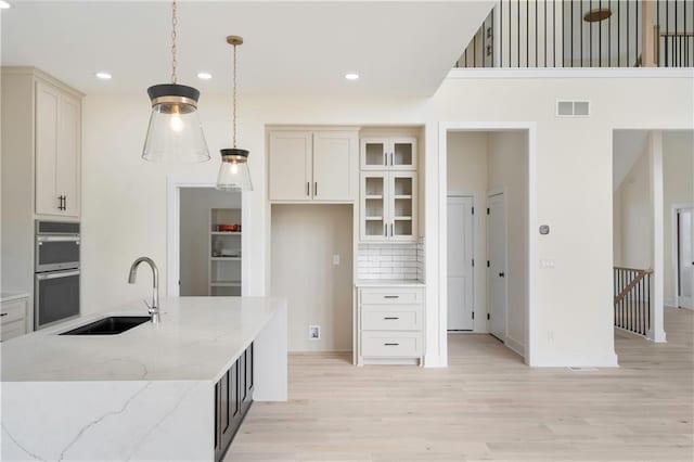 kitchen featuring hanging light fixtures, light stone countertops, light hardwood / wood-style floors, double oven, and sink