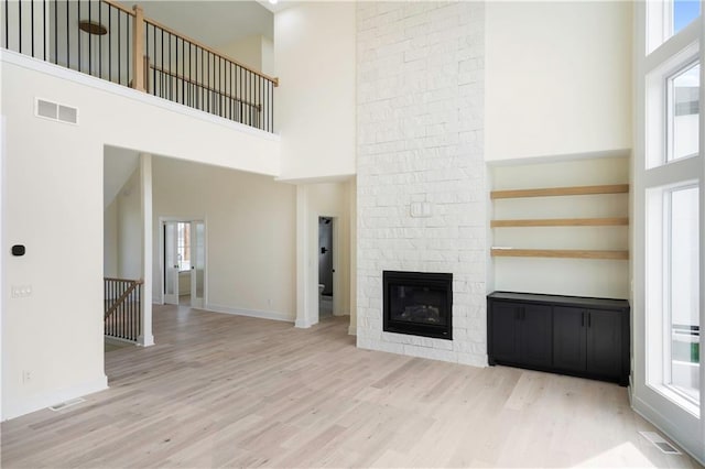 unfurnished living room with a stone fireplace, a towering ceiling, and light wood-type flooring