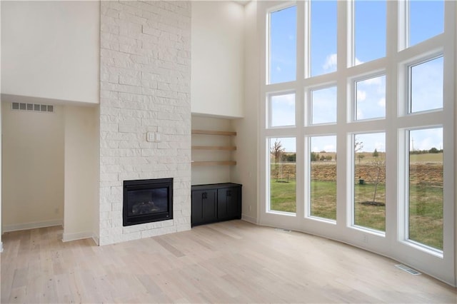 unfurnished living room with a towering ceiling, light wood-type flooring, and a fireplace