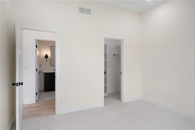 unfurnished bedroom with a spacious closet, light carpet, and a closet