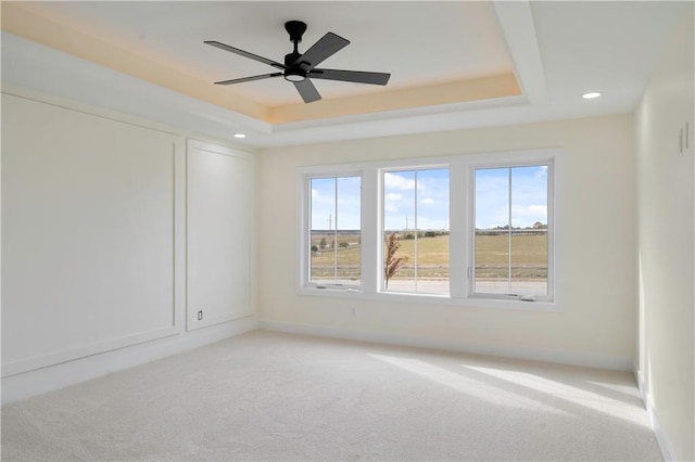 carpeted empty room featuring ceiling fan and a raised ceiling