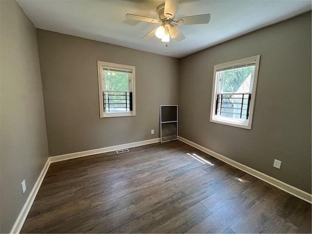 empty room featuring plenty of natural light, ceiling fan, and dark hardwood / wood-style flooring