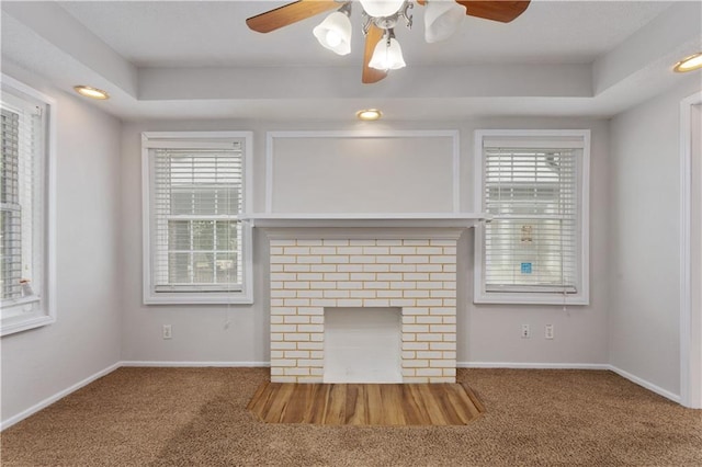 unfurnished living room with dark colored carpet, a tray ceiling, ceiling fan, and a fireplace