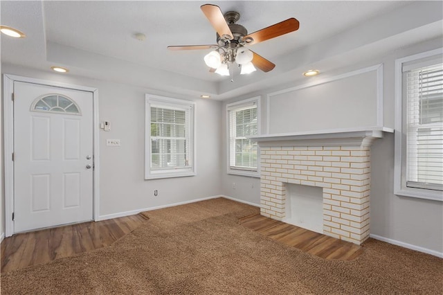 interior space with dark carpet, ceiling fan, a healthy amount of sunlight, and a brick fireplace