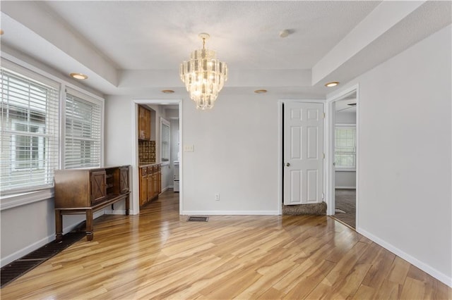 spare room with an inviting chandelier, a tray ceiling, and light wood-type flooring