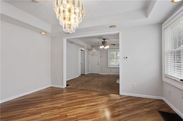 empty room featuring hardwood / wood-style floors, a tray ceiling, and ceiling fan with notable chandelier