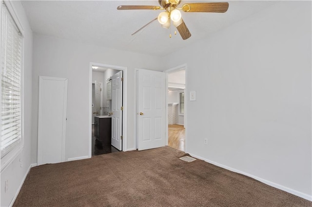 unfurnished bedroom with connected bathroom, dark carpet, and ceiling fan