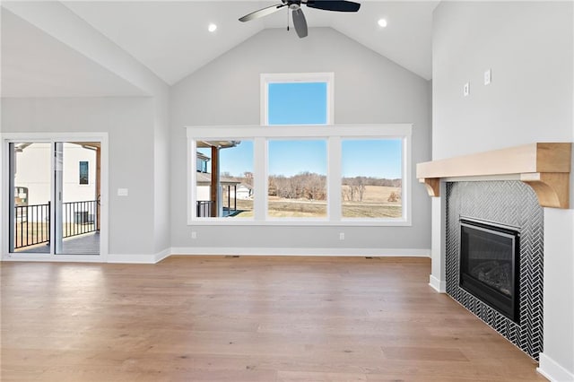 unfurnished living room featuring a tiled fireplace, light hardwood / wood-style flooring, lofted ceiling, and ceiling fan