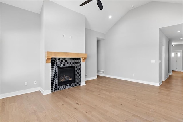 unfurnished living room with ceiling fan, lofted ceiling, a fireplace, and light wood-type flooring