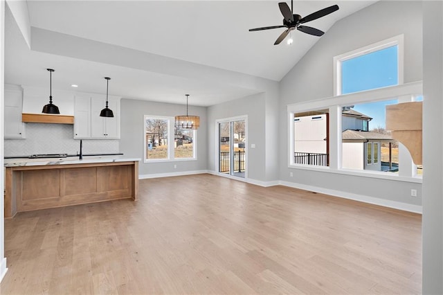 unfurnished living room featuring light hardwood / wood-style flooring, ceiling fan with notable chandelier, and a wealth of natural light