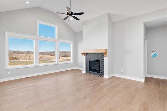 unfurnished living room featuring lofted ceiling, a tile fireplace, ceiling fan, and light wood-type flooring