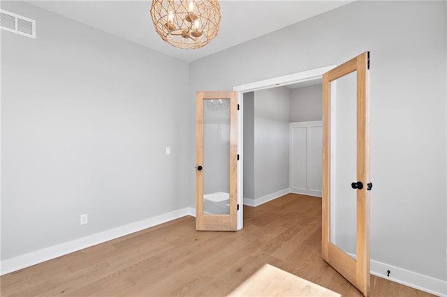 unfurnished bedroom with french doors, light hardwood / wood-style flooring, and a notable chandelier