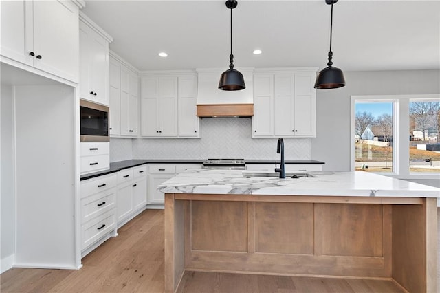 kitchen with decorative light fixtures, a kitchen island with sink, and white cabinets