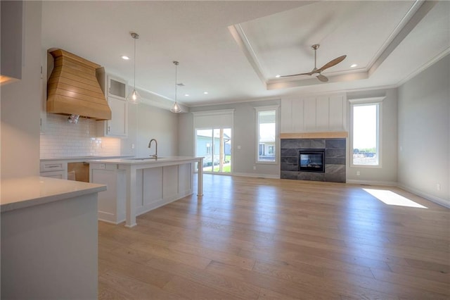 kitchen with premium range hood, decorative light fixtures, white cabinets, a raised ceiling, and plenty of natural light