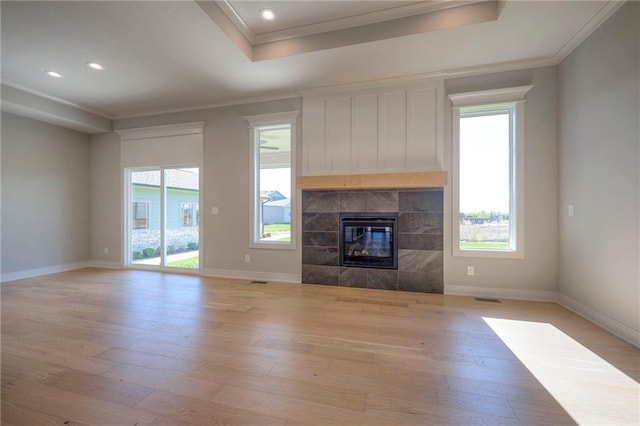 unfurnished living room with a tile fireplace, crown molding, light wood-type flooring, and a tray ceiling