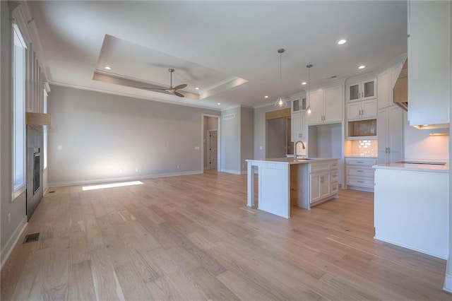 kitchen featuring white cabinetry, a tray ceiling, an island with sink, and light wood-type flooring