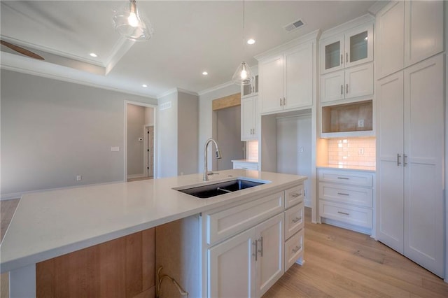 kitchen with hanging light fixtures, white cabinetry, sink, and an island with sink