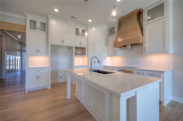 kitchen featuring white cabinetry, sink, an island with sink, and custom range hood