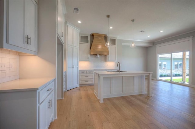 kitchen with decorative light fixtures, sink, white cabinets, custom exhaust hood, and a kitchen island with sink